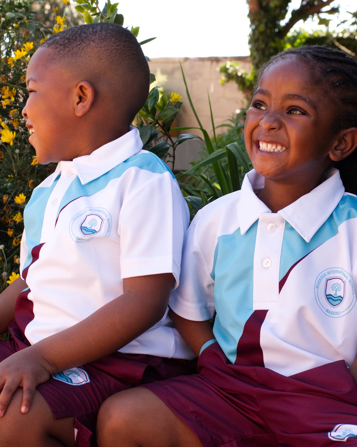 Two Riverside pupils in school sports kit, sitting together in the garden